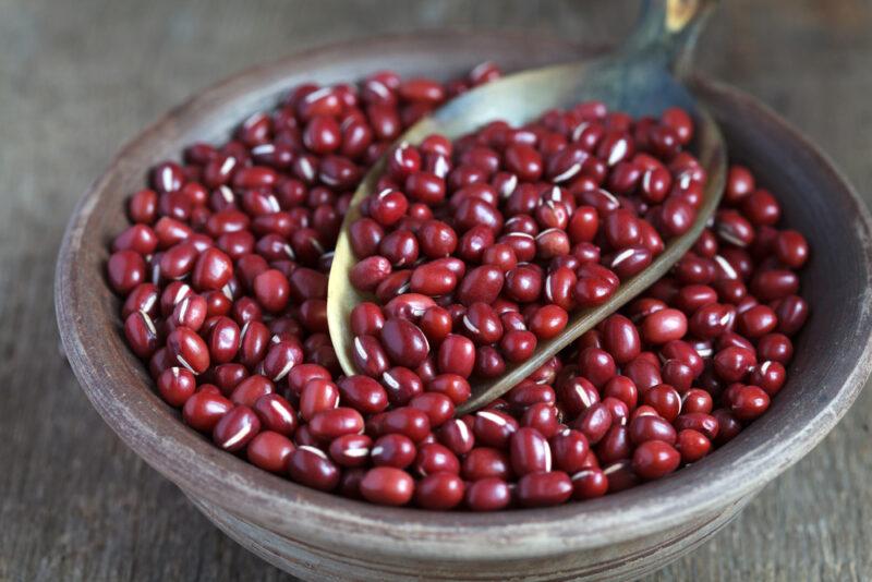 a closeup image of a clay bowl with adzuki beans or red beans resting on a wooden surface