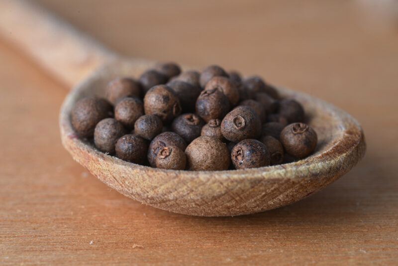 on a wooden surface is a wooden ladle full of allspice