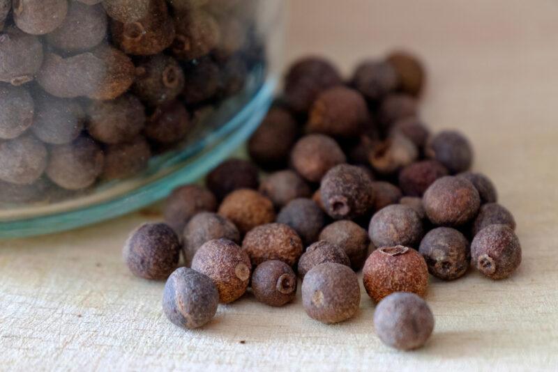 on a wooden surface is a closeup image of a dish with allspice, with loose allspice beside it