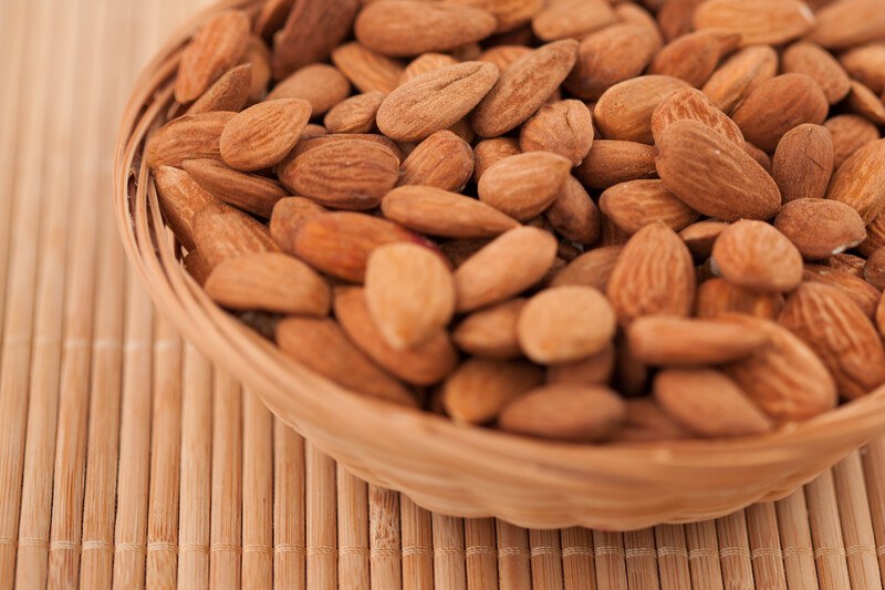 A small wicker basket filled with shelled almonds rests on a bamboo mat.