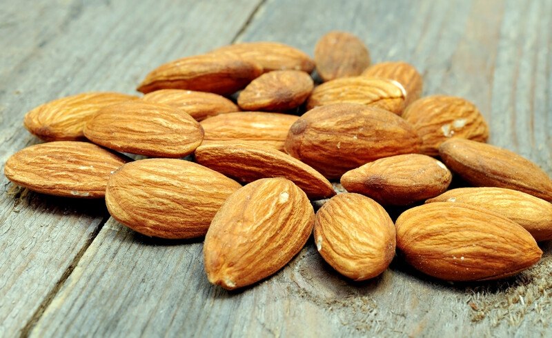 A handful of shelled almonds rests on a rustic wooden tabletop.