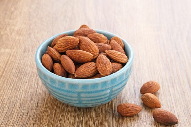 on a wooden surface is a small blue bowl full of almonds with a few loose almonds beside it