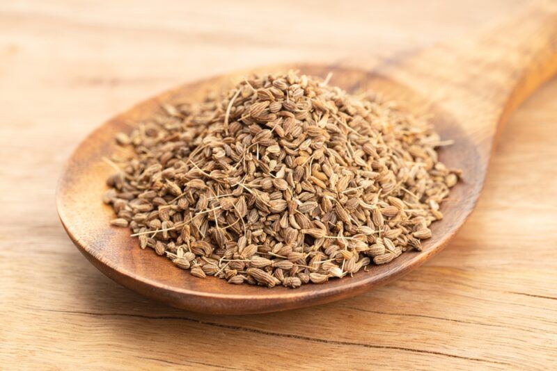 on a wooden surface is a closeup image of a wooden spoon with anise seeds