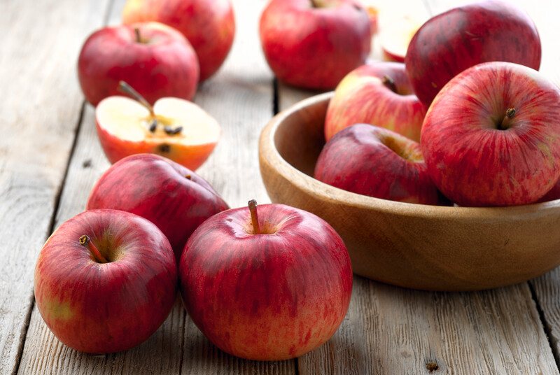 on a rustic wooden surface are apples with few of them in a wooden bowl