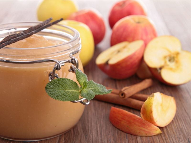 fresh apples, a jar of applesauce and cinnamon sticks on a wooden table.
