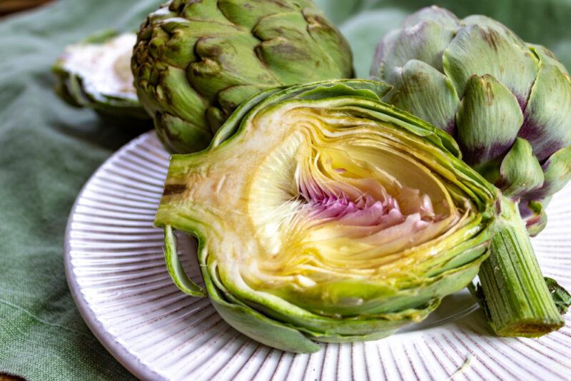 a closeup image of a white plate with three artichokes, one cut in half