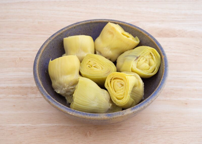 on a wooden surface is a light brown and blue ceramic bowl with artichoke hearts