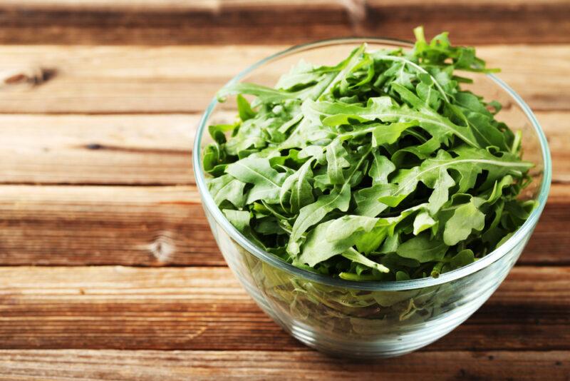 on a wooden surface is a clear glass bowl with arugula