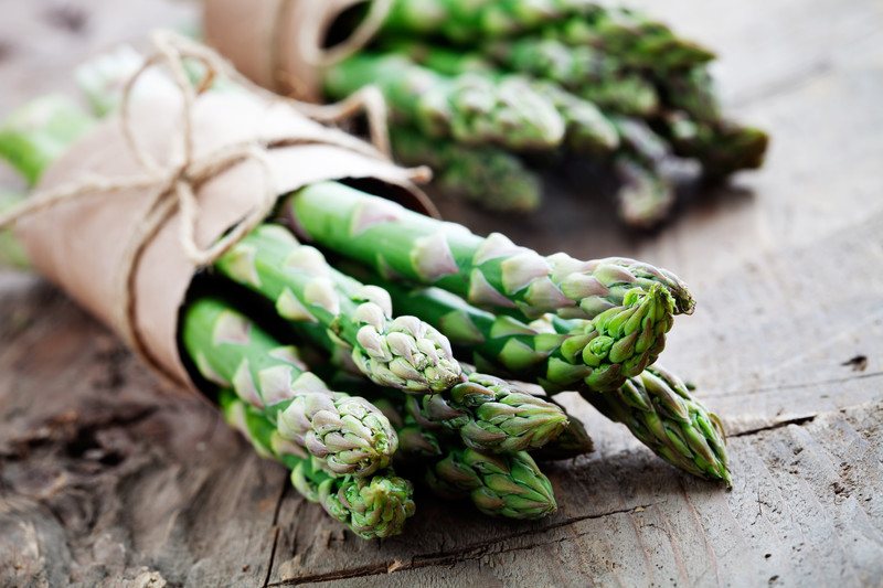 closeup shot of a wooden surface with a couple of bundled asparagus bound with a narrow brown paper and tied with an abaca string