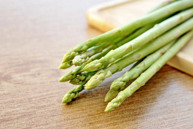 on a wooden surface is a bunch of fresh asparagus on a square brown dish