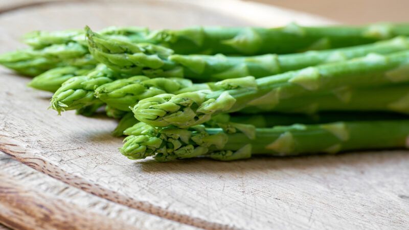 a closeup image of a bunch of asparagus on a wooden chopping board