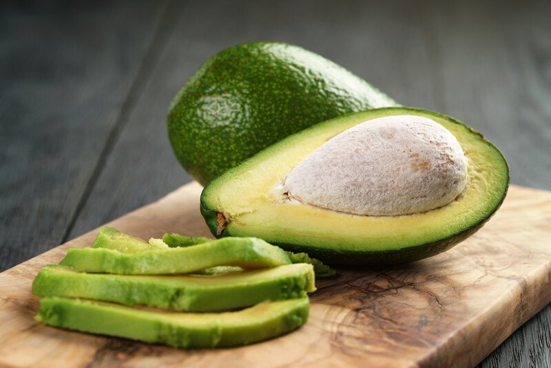 sliced avocado on a wooden board with a whole and halved avocado at the back