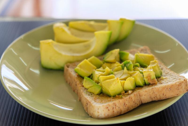 a closeup image of an olive green plate with sliced avocados and cubed avocados on a toast