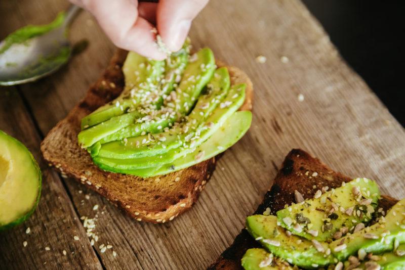 Two pieces of toast with sliced avocado and seeds on top