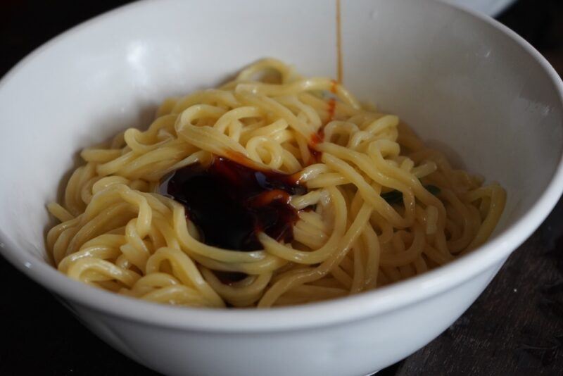 closeup image of a white bowl with bakmi noodles with a thick soy sauce