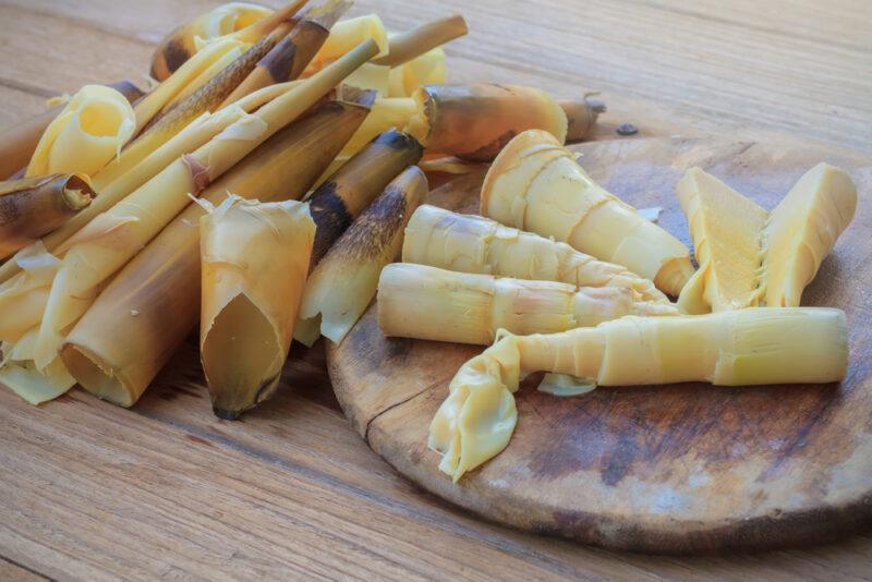 on a wooden surface is a small pile of bamboo shoots beside a round wooden chopping board with bamboo shoots as well