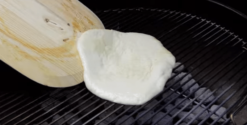 placing raw pizza dough with olive oil on a charcoal grill