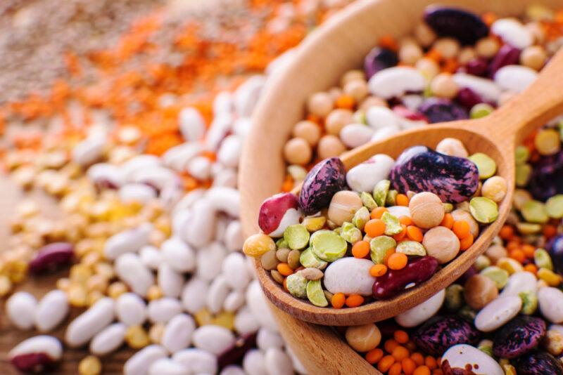 closeup image of  bowl of legumes with wooden spoon on top, around it are loose legumes as well