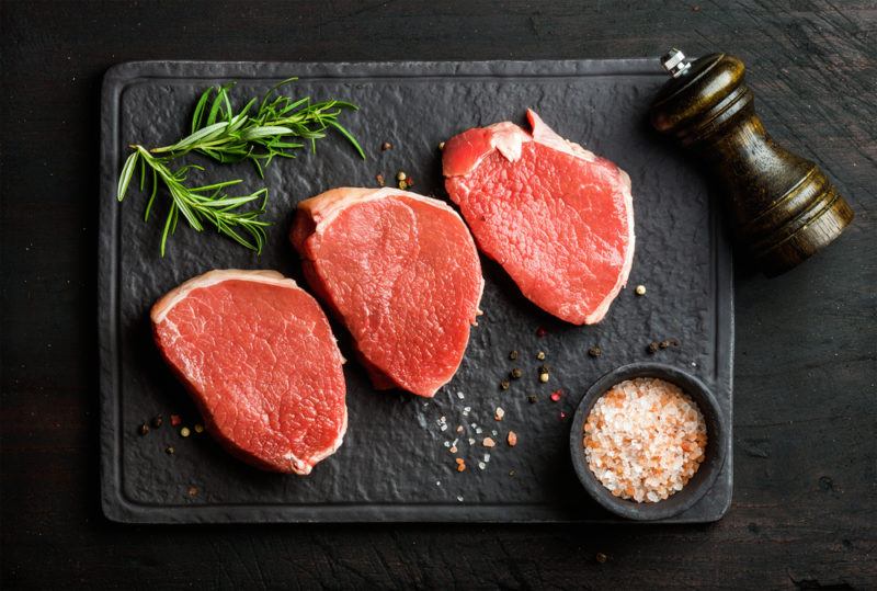 beef round eye steak raw on stone cutting board with coarse salt