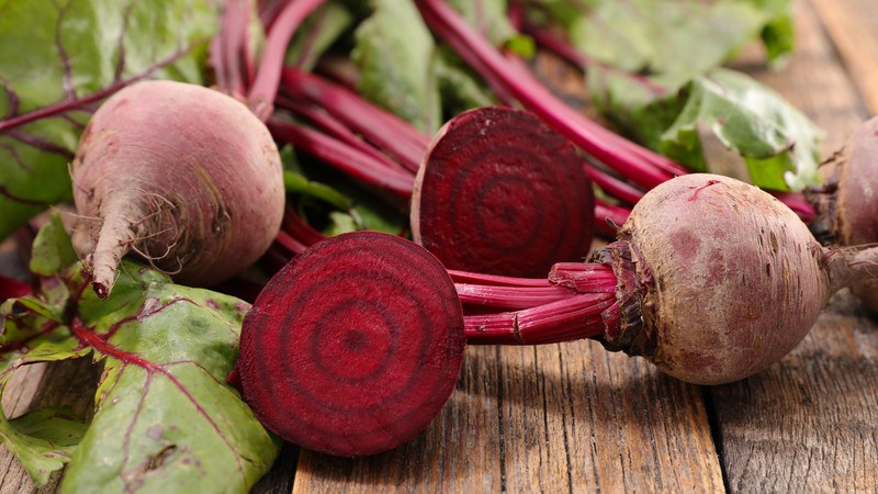 closeup image of beetroots with leaves, one cut in half, laid out on a wooden surface