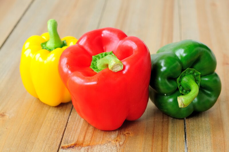 laid out on a wooden surface are fresh yellow, red, and green peppers 