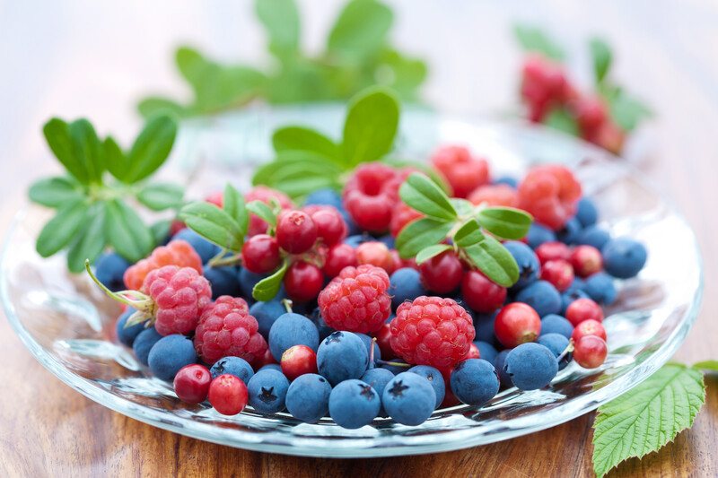 a closeup image of a clear glass plate full of berries with sprigs of herbs