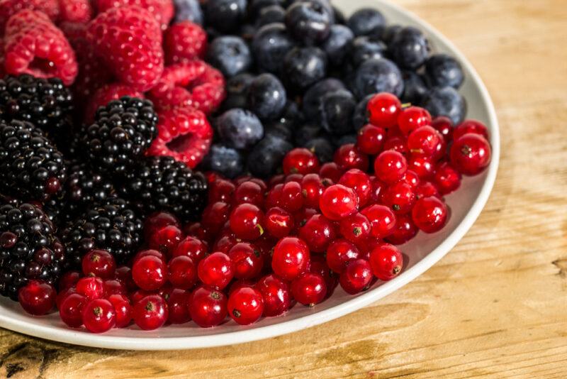 on a wooden surface is a white dish full of different berries including raspberries, blackberries, red currants, and blueberries