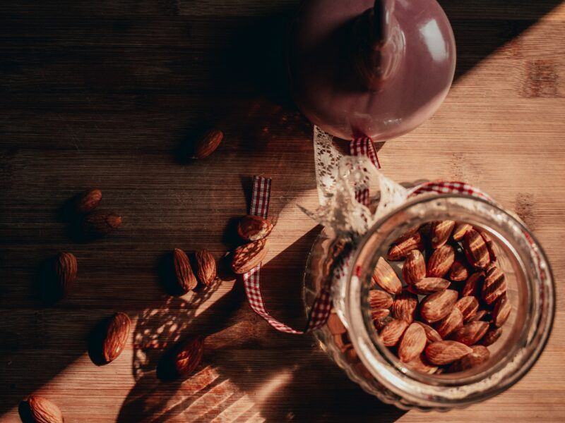 a top view of a jar filled with almonds with more almonds spilling onto the table to represent the best amaretto liqueur 
