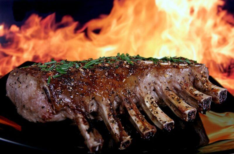 Cooked ribs in the foreground and fire in the background, highlighting the idea of beef protein powder