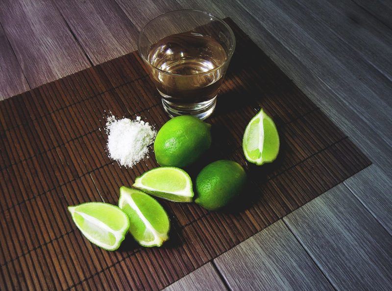 a shot of blanco tequila with salt and lime wedges surrounding the glass 