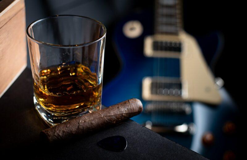 a glass of whiskey neat and a cigar on the table with a blurred guitar in the background to represent the best bourbon whiskey