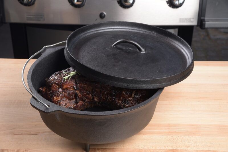 a black Dutch oven on a table with a big piece of meat inside to represent the best Dutch oven brands