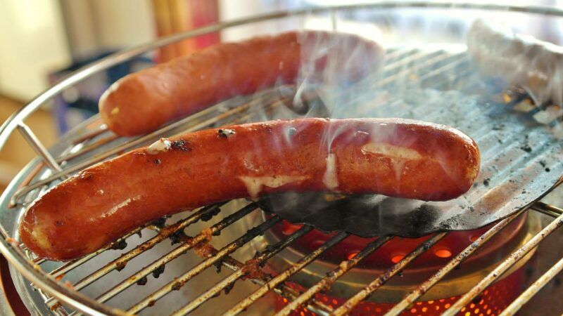 two hot dogs smoking on a grill to represent the best hot dog brands. 