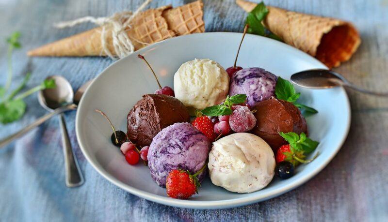 a bowl of multicolored ice cream with fruit and some cones in the background to represent the best keto ice cream brands
