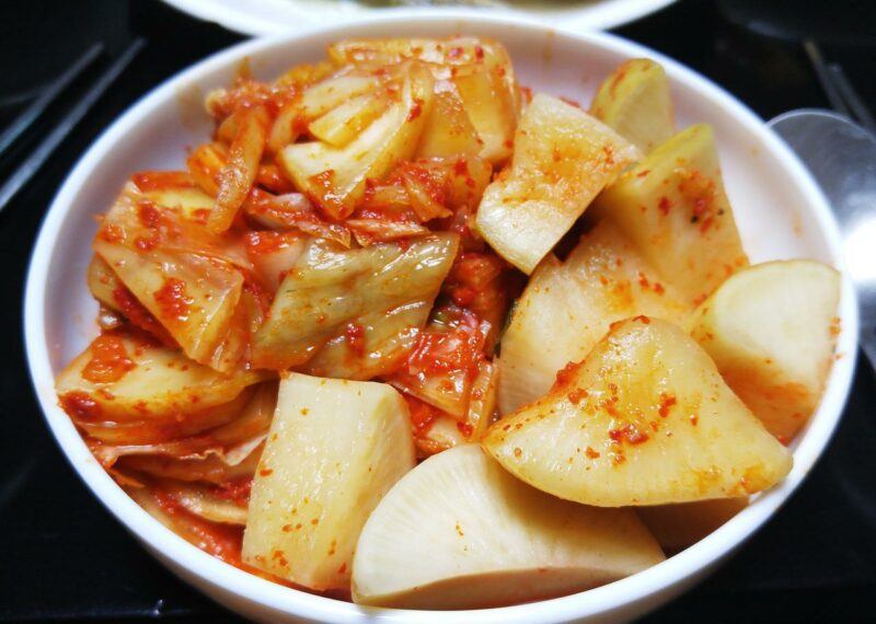 close up of a bowl of kimchi with utensils in the background to represent the best kimchi brands