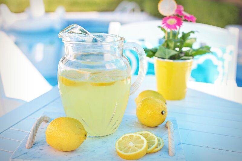 A pitcher of bright, lemon-infused liquid surrounded by lemons and lemon slices to represent the best limoncello liqueur 