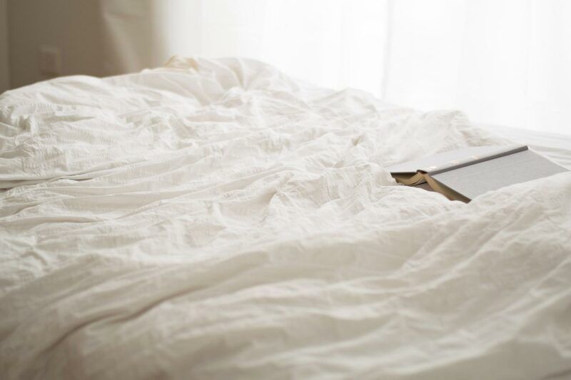 a cozy bed with natural lighting and an open book on it to represent the best melatonin brands 