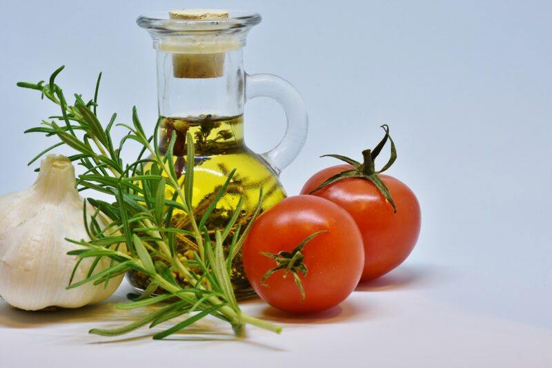 a small bottle of olive oil surrounded by veggie and herbs to represent the best olive oil brands