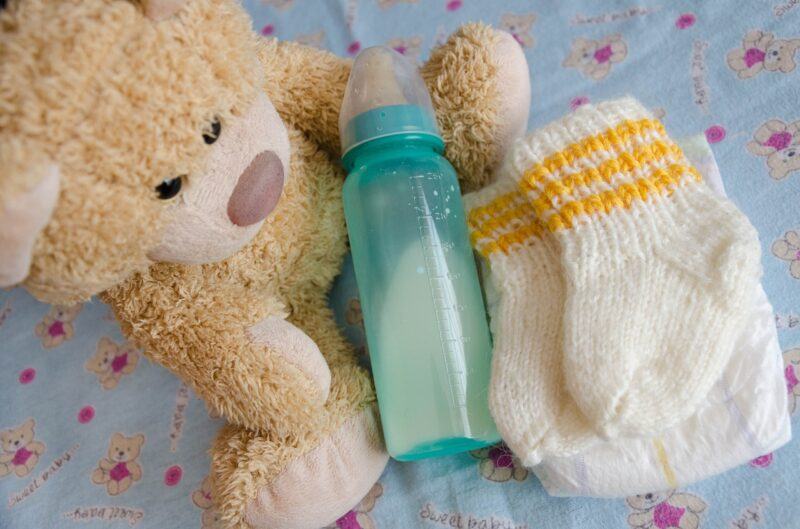 a teddy bear, knitted booties, and a bottle nestled together to represent the best plant-based baby formula