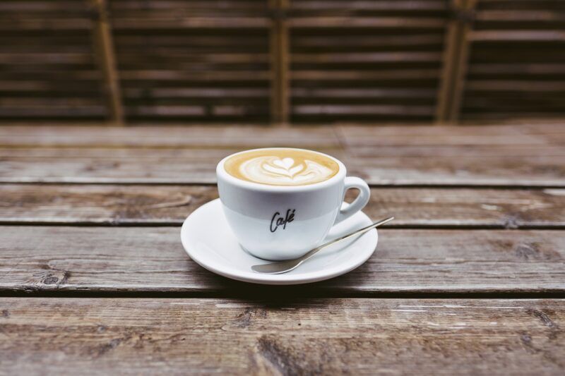 a cup of coffee on a saucer with a spoon next to it on a wooden table to represent the best plant-based coffee creamer 