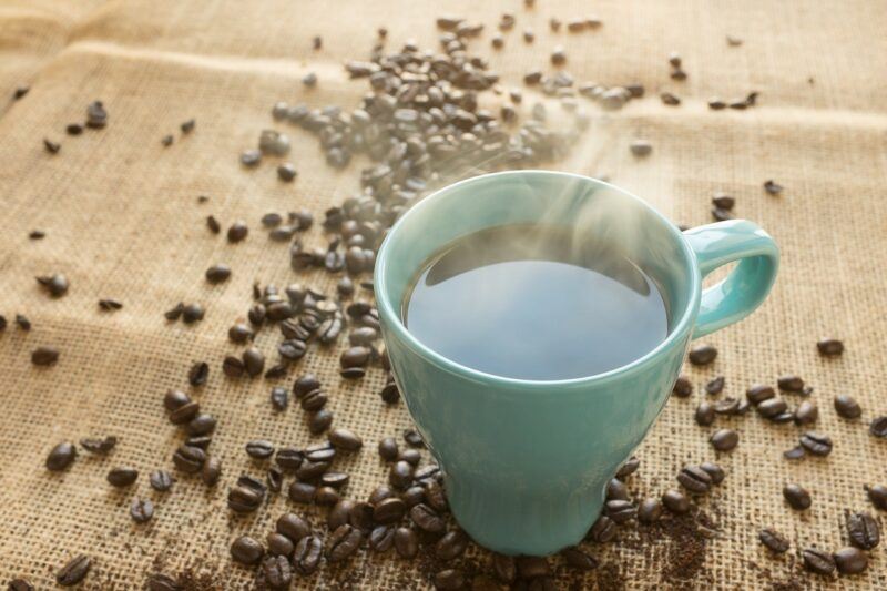 a steaming cup of coffee with scattered beans surrounding it to represent the best protein powder with caffeine