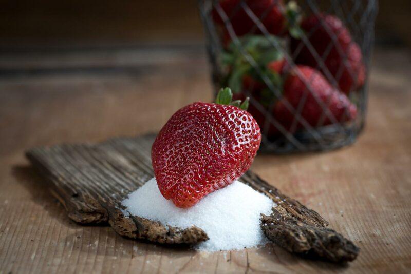 A strawberry sitting on a pile of sugar on top of a piece of bark to represent the best protein powder with real sugar 