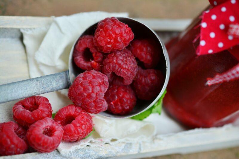 Fresh raspberries spilling out of a scoop next to a jar filled with raspberry drink to represent the best raspberry vodka