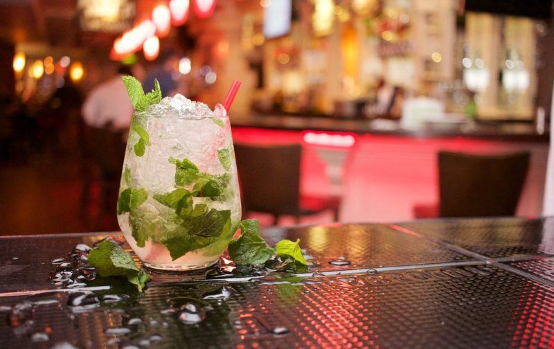 a mojito on a bar with some extra mint leaves around the glass to represent the best rum for mojitos 