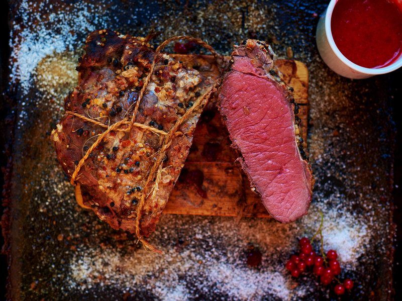 Sous Vide Beef  cooked perfectly evenly pink inside with salt and berry garnish on wooden block