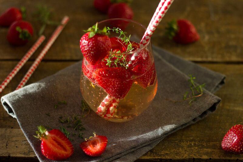 a small glass of clear liquid with strawberries floating in the glass and a red straw in it to represent the best tonics for gin