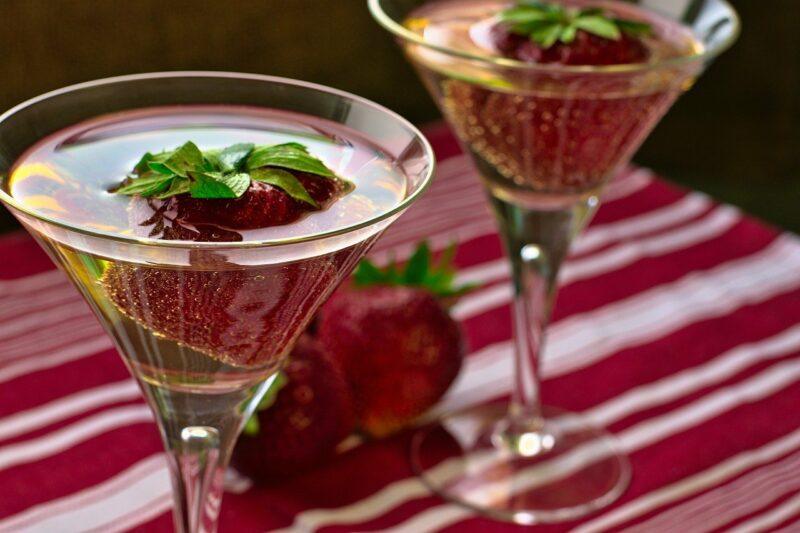 best-vermouth-for-a-vodka-martini | Food For Net two glasses of clear liquid garnished with strawberry on a red tablecloth to represent the best vermouth for vodka martinis