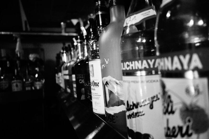 a black and white photo of many vodka bottles lines up on a shelf to represent the best way to store vodka