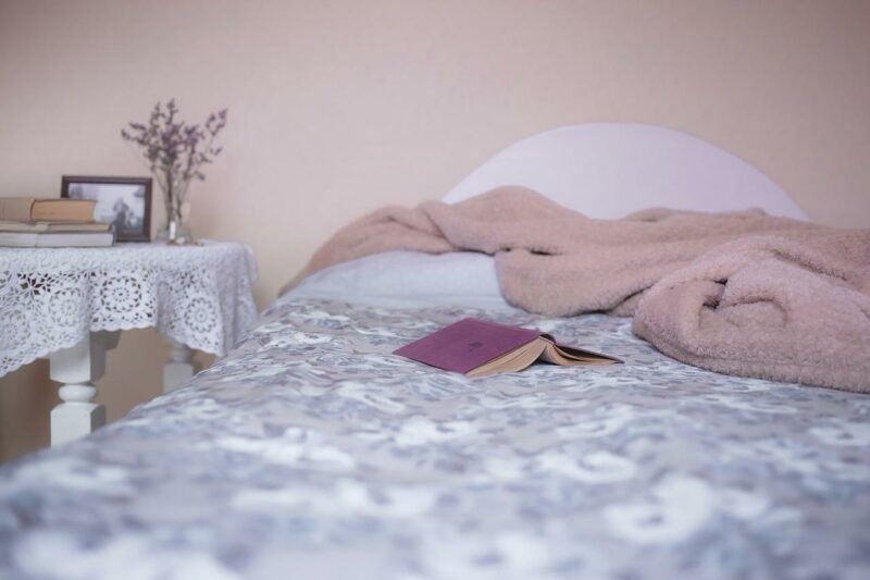 a bed with a brown throw blanket and an open book on it to represent the best weighted blanket brands