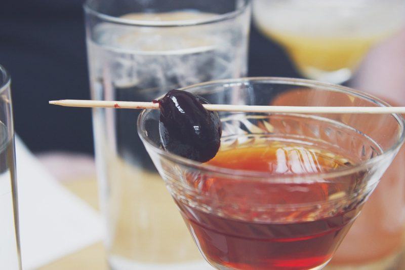 a close up of a Manhattan cocktail with other drinks in the background to represent the best whiskey for manhattans 